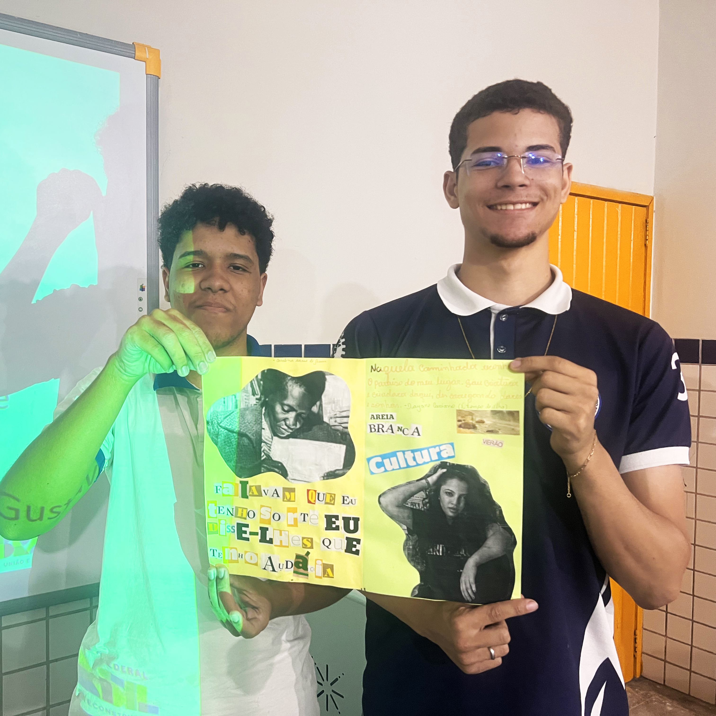 2 alunos sorrindo e exibindo cartaz com colagens de autoras